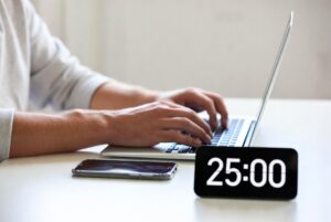 Minimal desk setup for deep work: person typing on laptop with phone face-down and a 25-minute focus timer running.